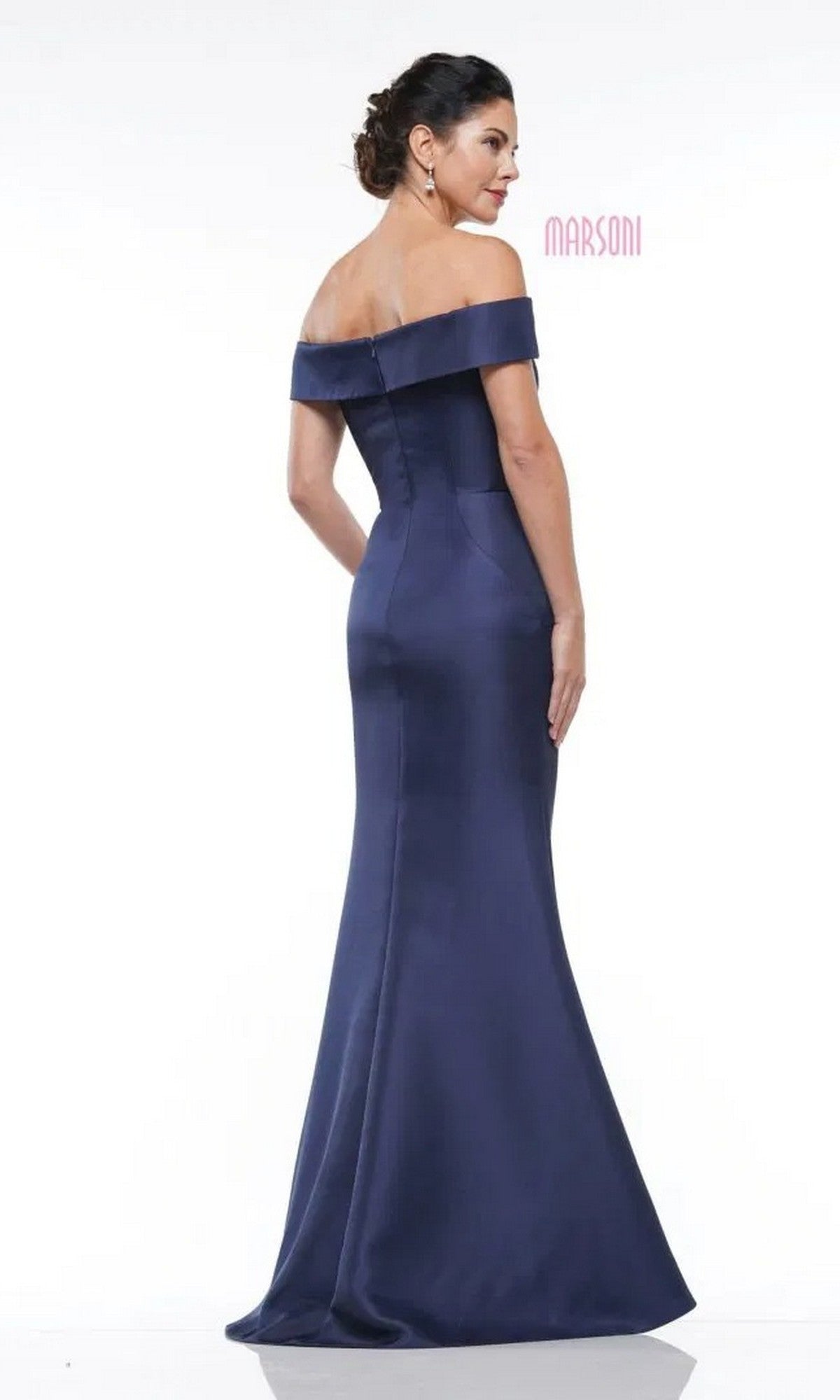 A woman models the Marsoni MV1003 long formal dress, a navy blue off-the-shoulder satin evening gown with beaded floral embellishments, posing against a plain white background and looking over her shoulder.